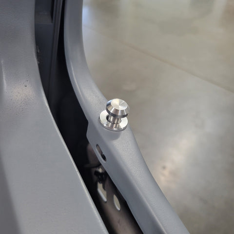 Close-up of a silver metallic mounting bolt or rivet attached to a curved gray metal frame, with a concrete floor visible in the background.