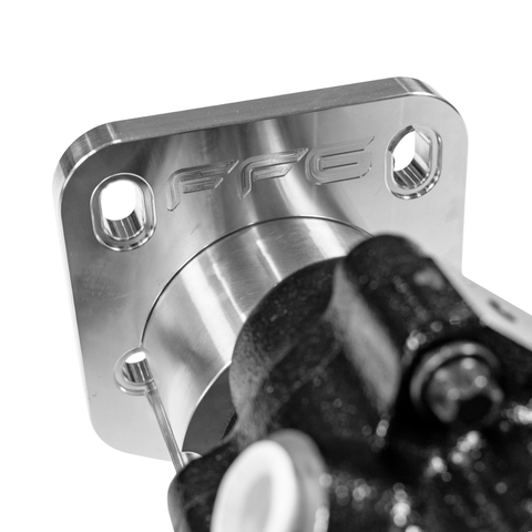 Close-up of a polished metallic mechanical component with a square flange, four bolt holes, and an embossed 'FFG' logo, shown against a white background with part of a dark metal assembly in the foreground.