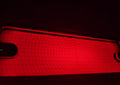 A close-up of a red illuminated tbrak light with circular concentric markings, shown against a dark background.