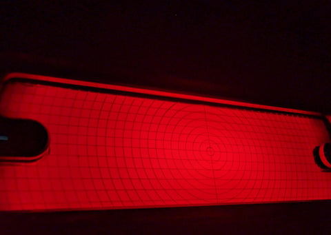 A close-up of a red illuminated tbrak light with circular concentric markings, shown against a dark background.