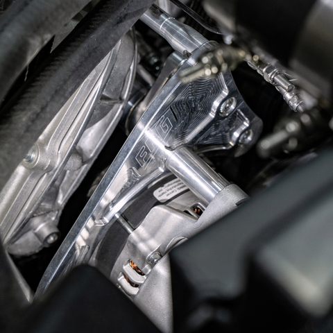 Close-up of a polished metallic engine component with visible branding and mechanical parts in a dark engine bay.