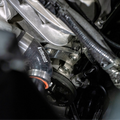 Close-up of an automotive engine component with a black and silver Vibration Control Damper (VCD) assembly, a black Vibration Isolation Hose, and a black pulley belt system.