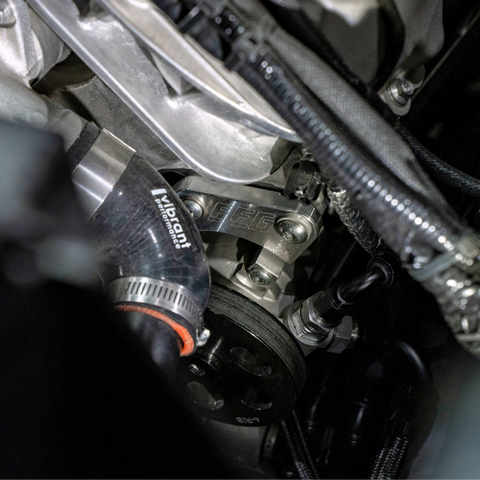 Close-up of an automotive engine component with a black and silver Vibration Control Damper (VCD) assembly, a black Vibration Isolation Hose, and a black pulley belt system.