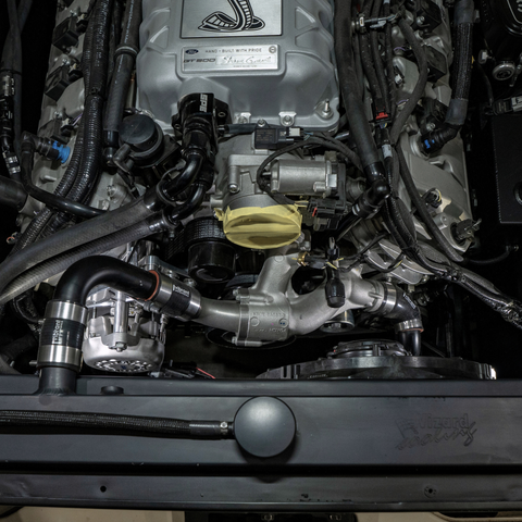 Close-up of a Ford V8 engine bay with a custom polished silver engine block, black hoses, and a yellow oil cap, photographed from above.